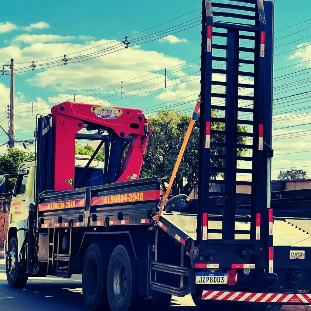 Caminhão Munck com plataforma e guindaste vermelho, visto de trás em uma rua ensolarada.